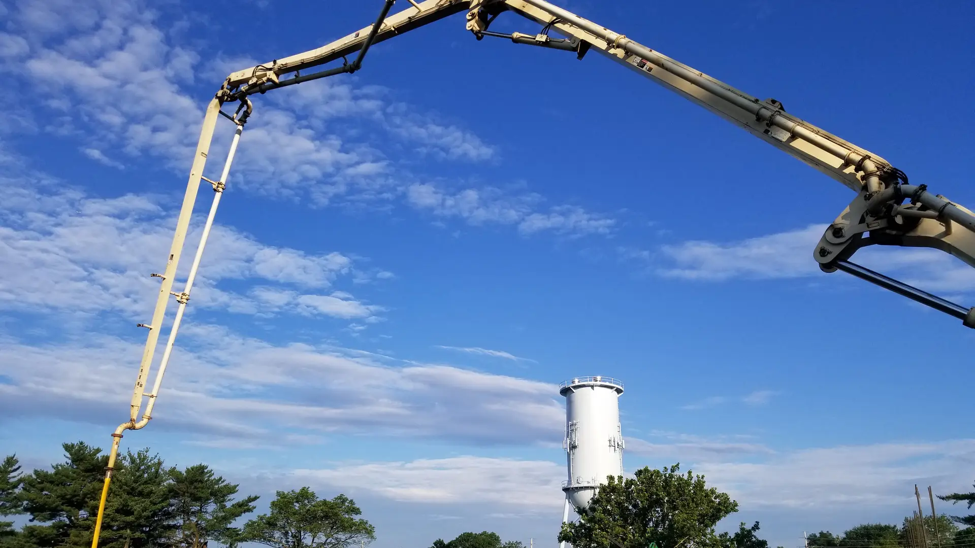 A&S boom pump arm arching across a blue sky over a job site