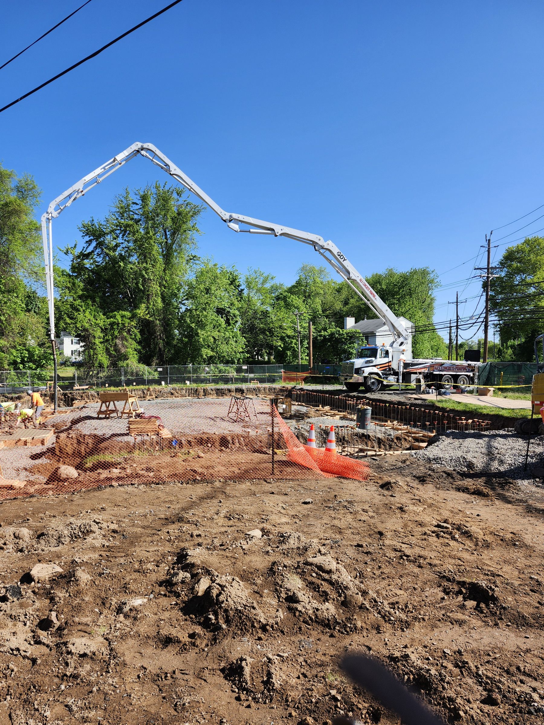 A&S DY boom pump at the street, reaching across an excavated site to a footing pour