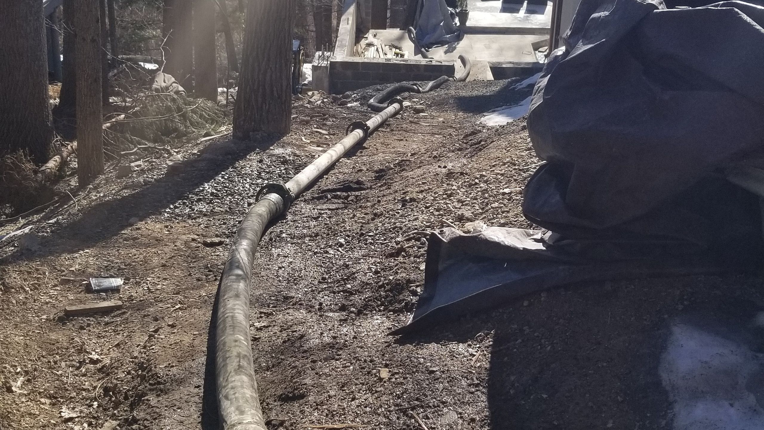 Concrete line pump hose running down a wooded slope beside a house