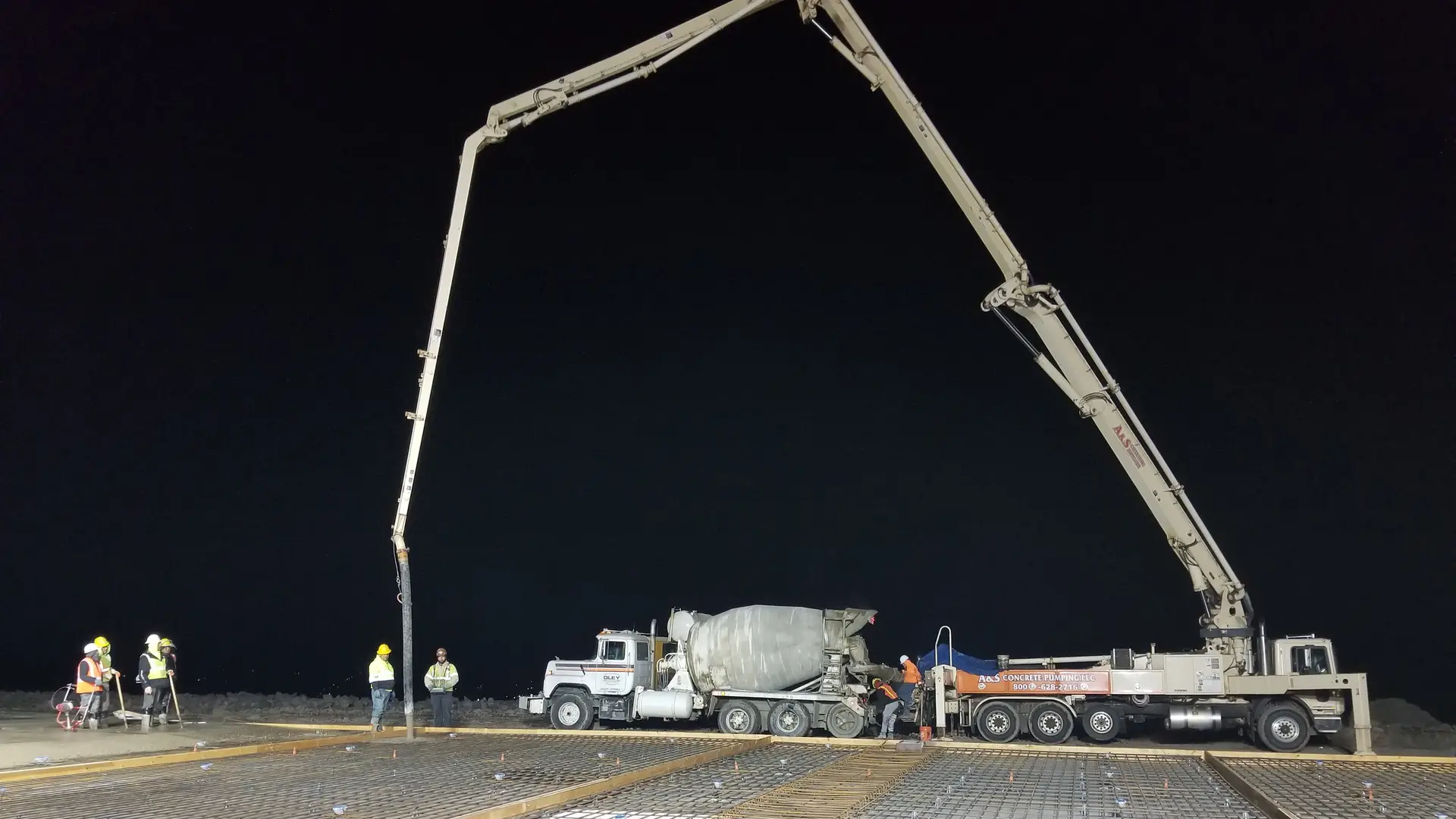 Boom pump placing a large slab at night under work lights, ready-mix truck at the pump