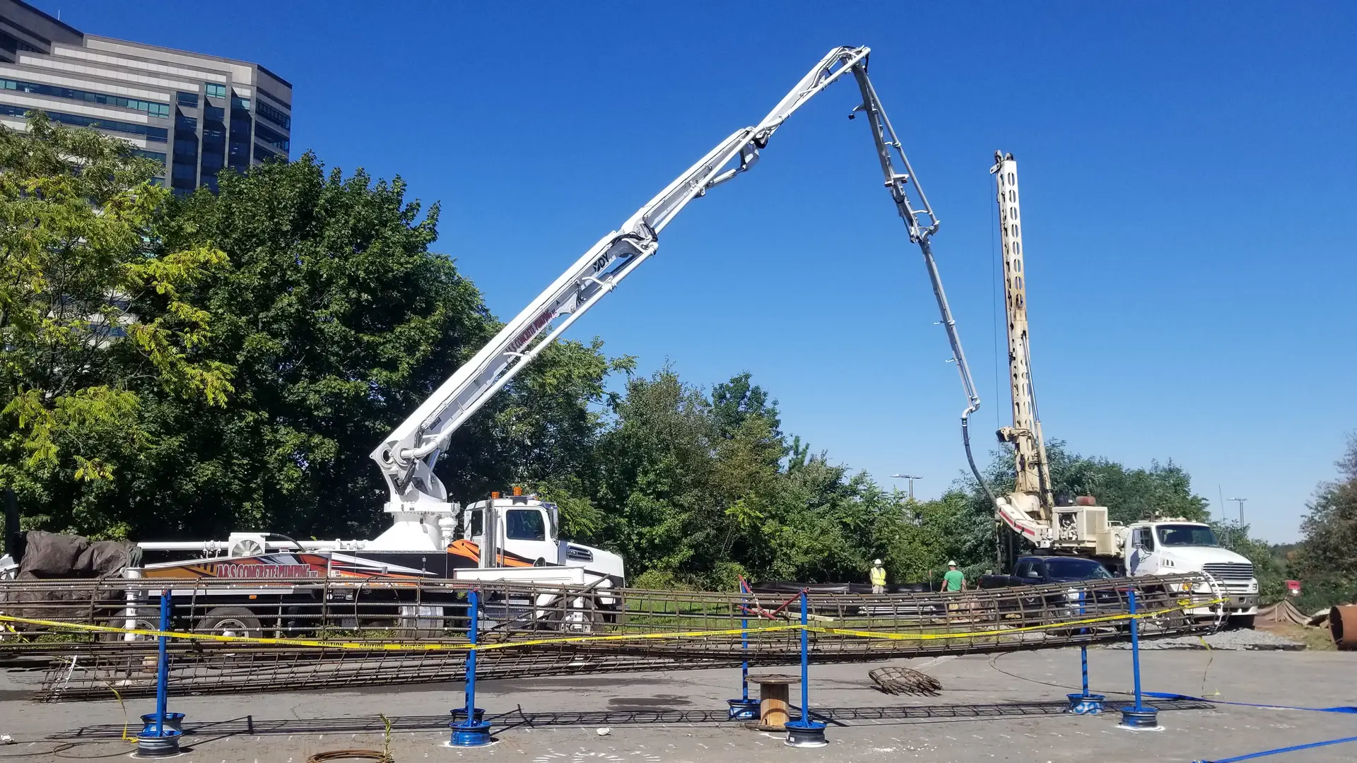 Two boom pumps set up on their outriggers on a job site beside an office park