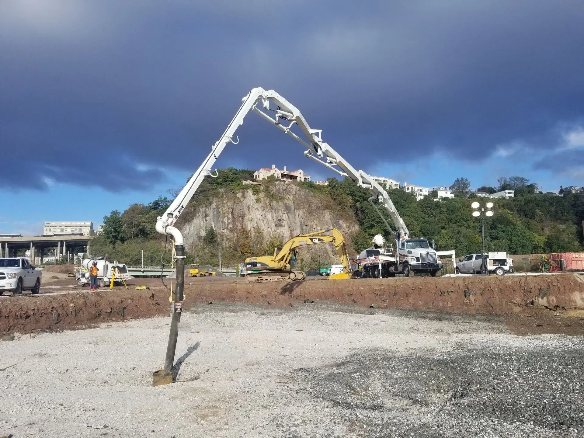 Concrete boom pump arching over a foundation site, the end hose lowered into a pile casing