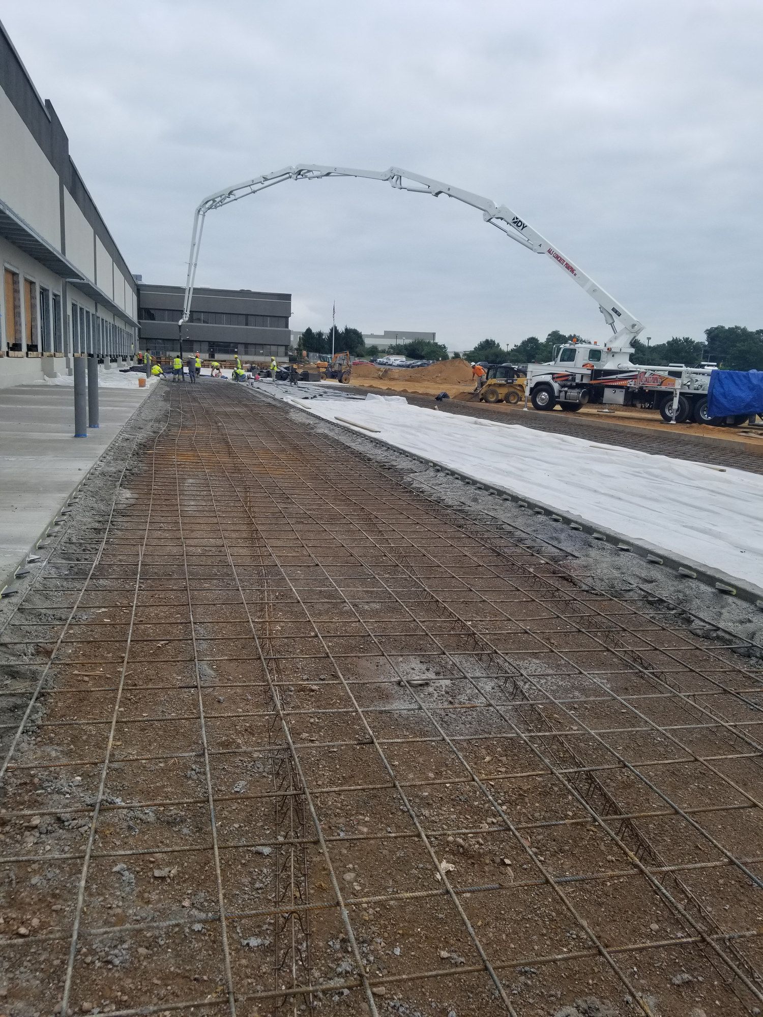 A&S boom pump placing concrete along a long reinforced slab beside a warehouse